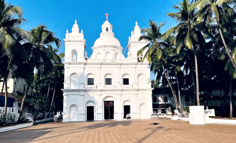 St Alex Church, Calangute: a white Portuguese-Goan church with twin towers and a dome, framed by coconut palms.